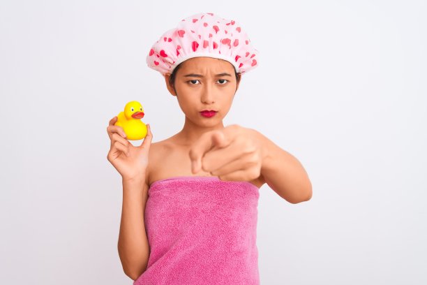 一名中国妇女穿着浴巾和帽子，拿着鸭子玩具，在孤立的白色背景下，手指指着相机和你，手势，正面自信的手势图片下载