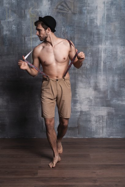 帅气的家伙时尚性感的年轻大胡子男子模型与裤带上的灰色背景。图片下载
