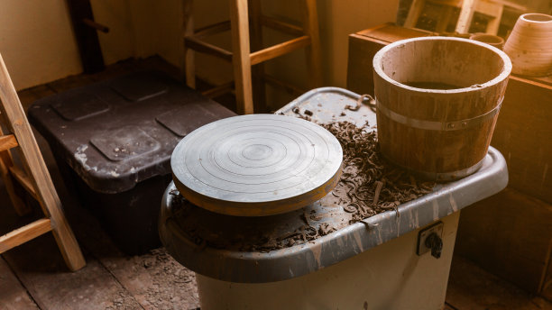 陶轮机器，用于制作手工制作的陶瓷，如碗，盘子和杯子在前景与木桶。创意工作室。图片下载