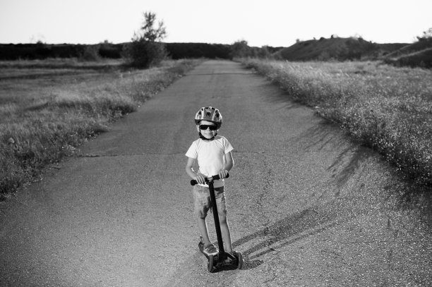 黑白可爱的小白种人男孩戴着太阳镜和蓝色运动头盔站在摩托车上沙漠柏油路户外休闲图片下载