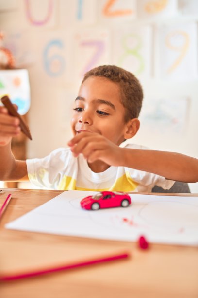 美丽的非洲裔美国学步儿童坐在油漆汽车玩具使用记号笔在书桌上在幼儿园图片下载