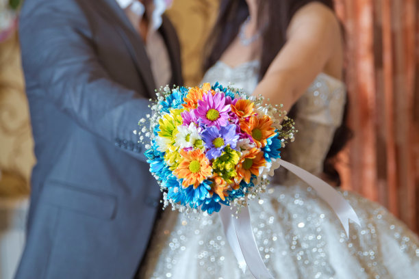 他手里拿着一朵结婚花。彩色微距照片详细的花束与色彩丰富的玫瑰，白色的小花和假钻石在玫瑰的中心。图片下载