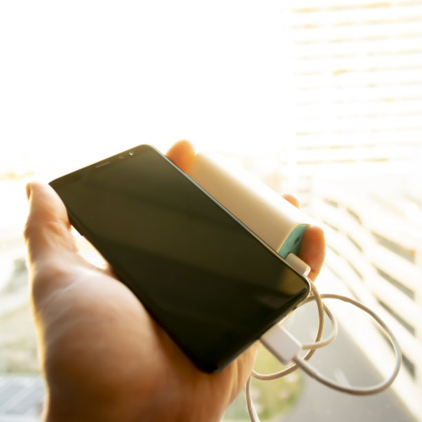 手拿着黑色的智能手机(手机)，正用电池充电，阳光透过窗户照射进来图片下载