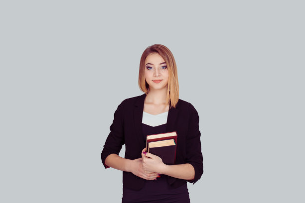 面带微笑的学生背着书包，拿着一堆书孤立的灰色背景图片下载