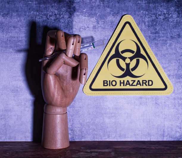 木制手拿温度计，背景上有生物危害标志。COVID-19概念图片下载