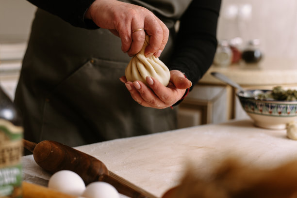 成年女厨师裹着围裙，把碎肉裹在面团里。一个女人正在做khinkali并捏面团图片下载