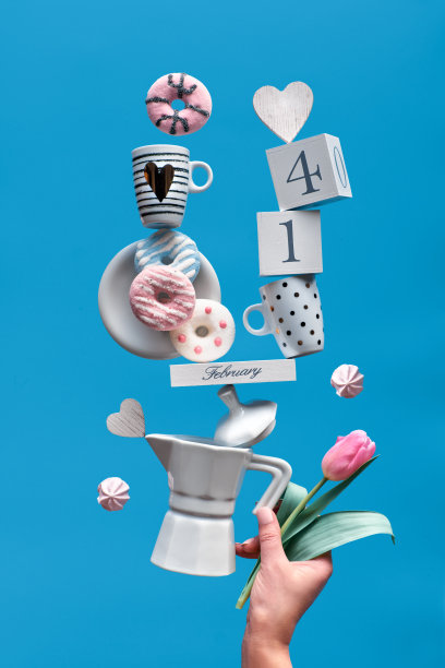 情人节有趣的背景在蓝色薄荷。木历2月14日，上面有咖啡杯、郁金香、粉色甜甜圈和棉花糖。女性手握平衡金字塔。图片下载