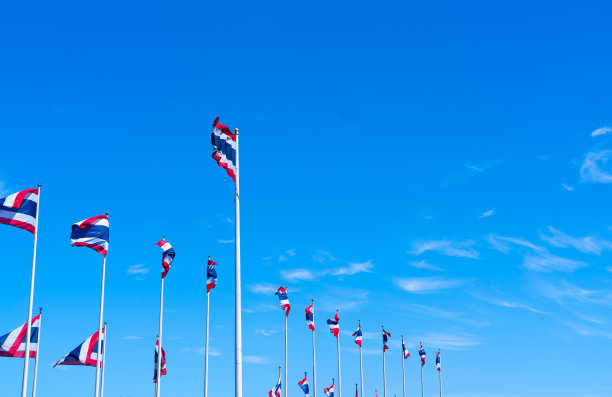 许多泰国国旗在蓝色的天空中飘扬。一面泰国国旗被拉到旗杆顶端。红、蓝、白三色长方形织物。泰国王国国旗。图片下载