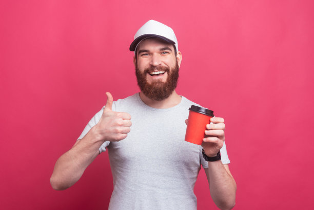 一张长着胡子的快乐男子的照片，他竖起大拇指，拿着一杯咖啡要走图片下载
