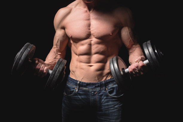 英俊有力的运动员，带着哑铃自信地向前看。强壮的健美运动员有六块腹肌，完美的腹肌，肩膀，二头肌，三头肌和胸部。力量和动力图片下载