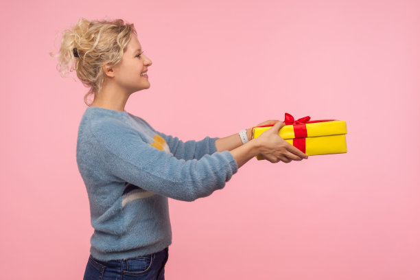 侧面观看善良的快乐女人与短卷头发在温暖的毛衣送礼物盒和微笑图片下载