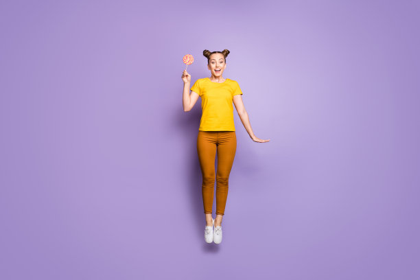 完整的身体尺寸照片，欢快积极可爱可爱迷人的女朋友跳兴奋的感觉后，品尝她的糖果，穿着棕色的裤子，鞋子孤立在紫色的柔和的颜色背景图片下载