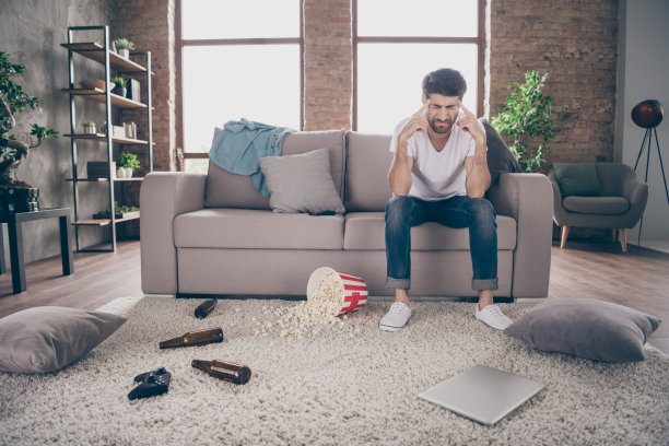 混血儿的照片，男人坐在沙发，抱着寺庙，喝醉了啤酒瓶爆米花地板有疯狂的stag party，宿醉，早上头痛，凌乱的公寓室内图片下载