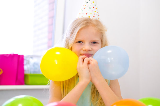 金发白人女孩的肖像在照相机生日派对微笑。节日色彩缤纷的背景与气球。垂直图图片下载