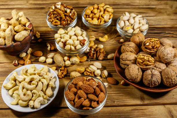 木桌上各种各样的坚果。杏仁，榛子，开心果，花生，核桃和腰果放在小碗里。健康饮食的概念图片下载