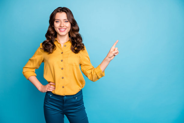 惊人的波浪女士的照片指示手指空的空间建议新产品低折扣价格穿黄色衬衫裤子孤立的蓝色背景图片下载