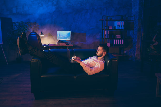 专注的高管的全长照片躺在黑色的皮沙发上用笔记本电脑工作读工作企业信息类型的项目演示，穿着白衬衫在黑暗的办公室他呆在晚上图片下载