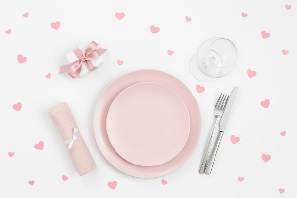 粉色的桌子上装饰着心形彩纸，礼物，白色背景上的餐巾。浪漫或婚宴。情人节或母亲节的背景。图片下载