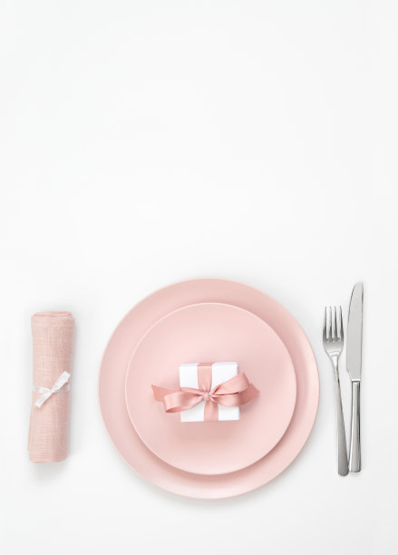 白色背景上的粉色餐具摆设，盘中放有礼物、餐巾和刀叉。浪漫婚礼晚宴，情人节背景。图片下载