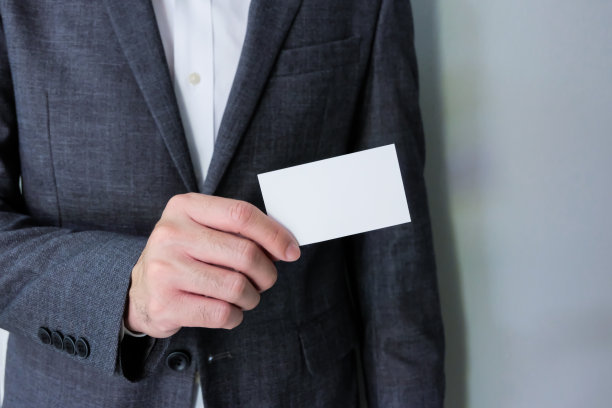 男士商务人士穿着灰色正装和白色衬衫拿着空白的白色名片模拟模板，把名字和文字放在上面。广告的经营理念，联系方式。图片下载