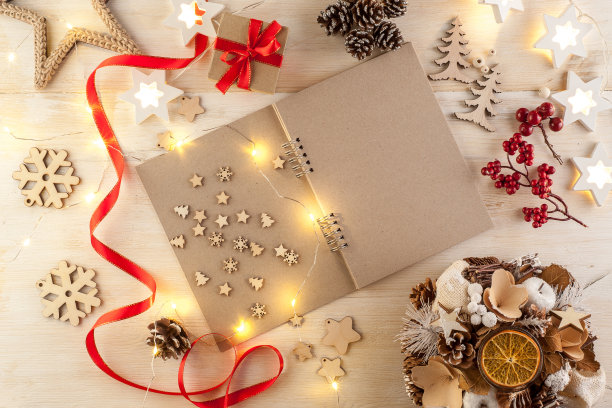 在一张木制桌子上，打开一个黑色的笔记本，周围是手工制作的圣诞装饰品图片下载