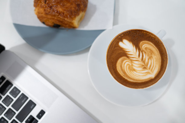 特写拿铁艺术咖啡杯与笔记本电脑键盘图片下载