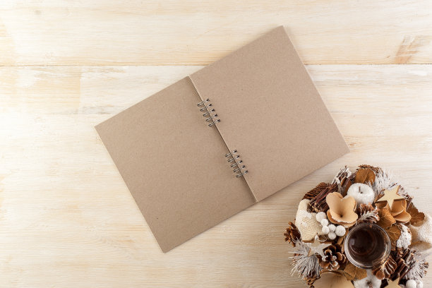 在一张木制桌子上，打开一个黑色的笔记本，周围是手工制作的圣诞装饰品图片下载