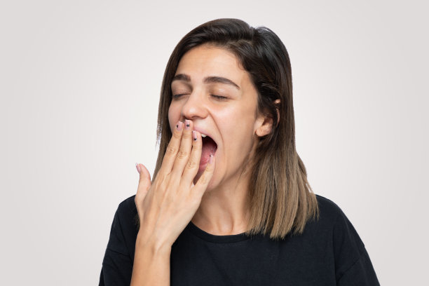 年轻女子越过孤立的背景打哈欠疲倦用手捂住嘴。图片下载