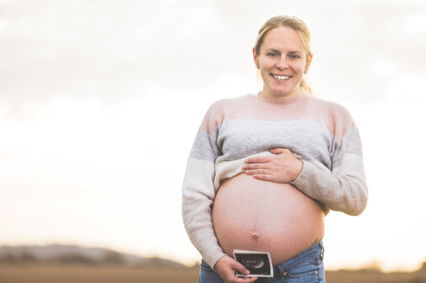 一位孕妇正拿着她宝宝的照片，超声波照片。在户外。图片下载
