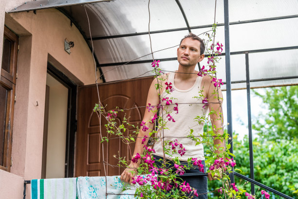 乡村别墅的家，农场小屋的别墅与年轻人站在欧洲的入口看爬粉红色的紫色的花图片下载