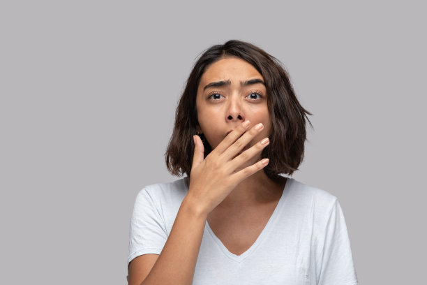 年轻女子越过孤立的背景打哈欠疲倦用手捂住嘴。图片下载