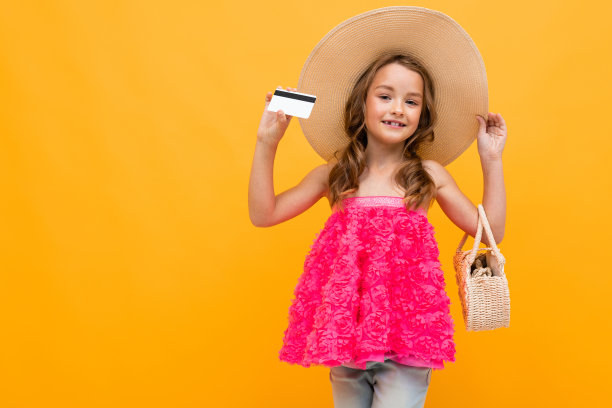 白人女孩戴着草帽，带着一个圆袋子，拿着一张黄色背景上的信用卡图片下载