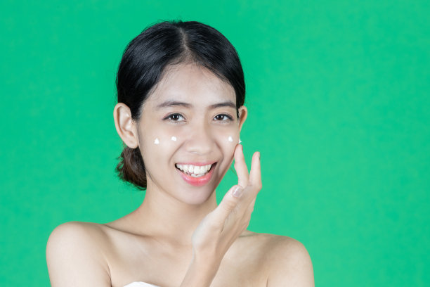 美丽健康的年轻亚洲妇女与面霜在绿色孤立的背景。化妆品护肤理念。图片下载