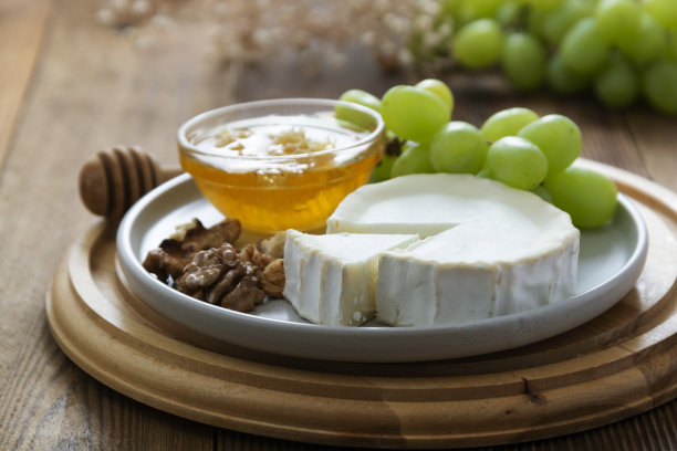 白色的，圆形的奶酪与蜂蜜，坚果和葡萄的背景。黑色食物的照片。图片下载