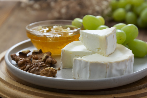 白色的，圆形的奶酪与蜂蜜，坚果和葡萄的背景。黑色食物的照片。图片下载