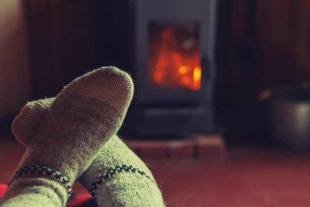 在壁炉背景下的冬季服装和羊毛袜中的双脚和腿。女人在寒冷的冬日或秋日夜晚坐在家里放松身心并取暖。冬季和寒冷天气概念。舒适的圣诞前夕图片下载