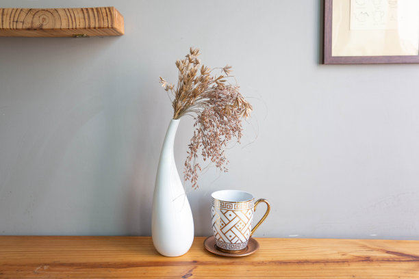 木桌上放着一个白色花瓶，花瓶上放着干花。客厅的灰墙。早....图片下载