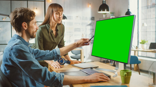 女艺术总监咨询设计师同事，他们工作的个人电脑与绿色屏幕模拟显示。他们在一个很酷的办公室阁楼工作。他们看起来很有创意和酷。图片下载