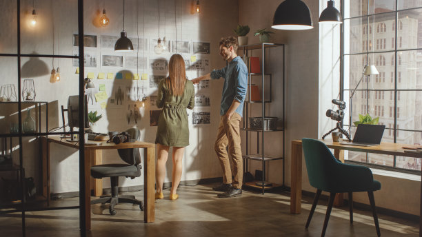 年轻有创造力的男性和女性正在整理他们办公室阁楼墙上的情绪板。图片代表未来的运动视频。同事们正在工作和讨论这个项目。阳光明媚的一天。图片下载