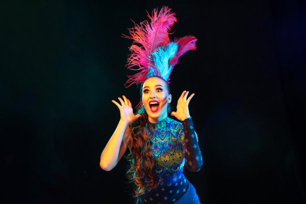 美丽的年轻女子在狂欢节和化妆舞会服装在彩色霓虹灯在黑色的背景图片下载