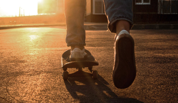 滑板腿近了，照片模糊了。一个穿着牛仔裤和运动鞋玩滑板的人在城市里玩。极端的城市运动。阳光摄影，胶片颗粒，分离。图片下载