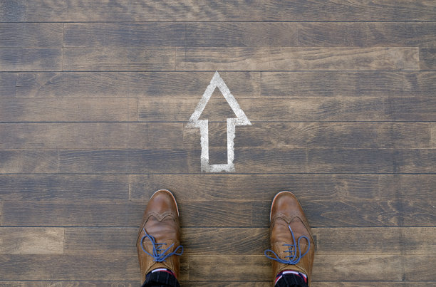 前进的道路:一个人站在木制地板上的箭头标志前图片下载