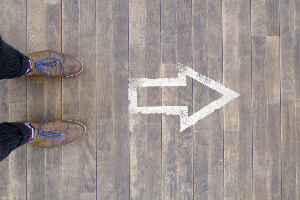 前进的道路:一个人站在木制地板上的箭头标志前图片下载