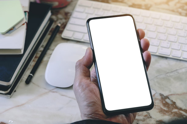 男子坐在办公桌前手持带空白屏幕的智能手机的局部照片图片下载