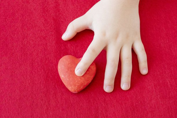 儿童的手在红色的背景上握住一颗红心，医疗保健，爱情，器官捐赠，家庭保险，世界心脏日，世界卫生日，母亲节，情人节图片下载