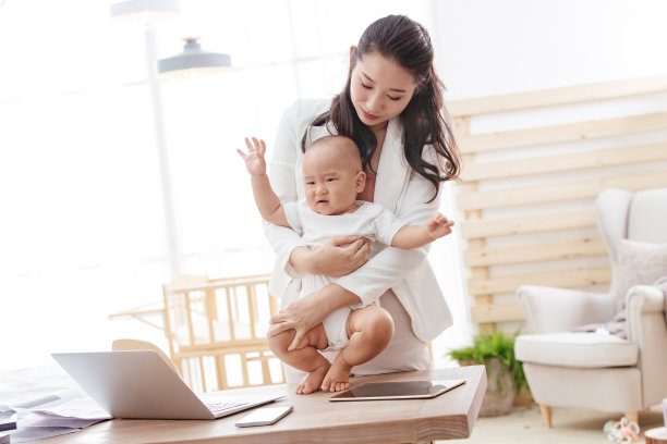年轻妈妈抱着孩子在家办公图片下载