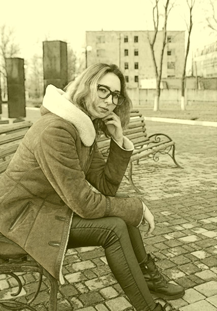 一个戴眼镜的女孩坐在公园长椅上等待约会，背景是冬天的城市风景。图片下载