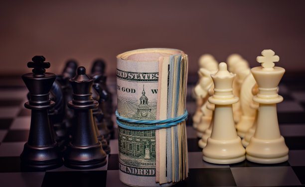特写扭曲美元站在棋盘之间的一个白棋和黑棋队。概念上的照片。团队游戏。竞争。图片下载