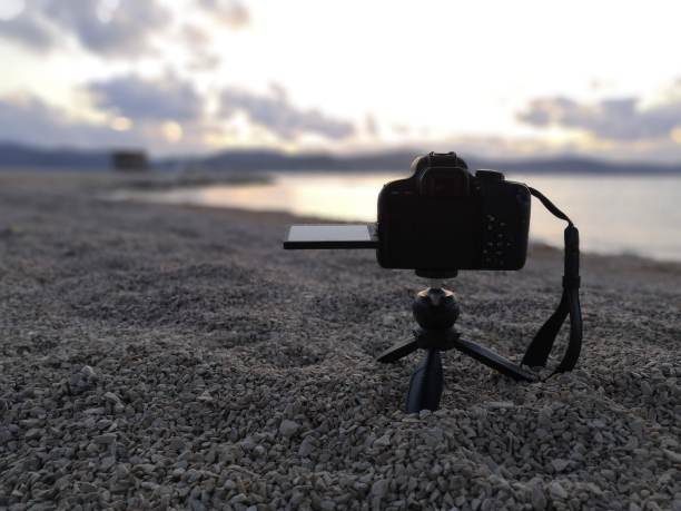 黑色的单反相机安装在沙滩上的一个小三脚架上，拍摄远处的大海和日落。黄色天空金色时光图片下载