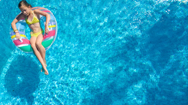 从游泳池空中俯瞰，孩子在充气甜甜圈上游泳，孩子在家庭度假胜地的蓝色海水中嬉戏图片下载